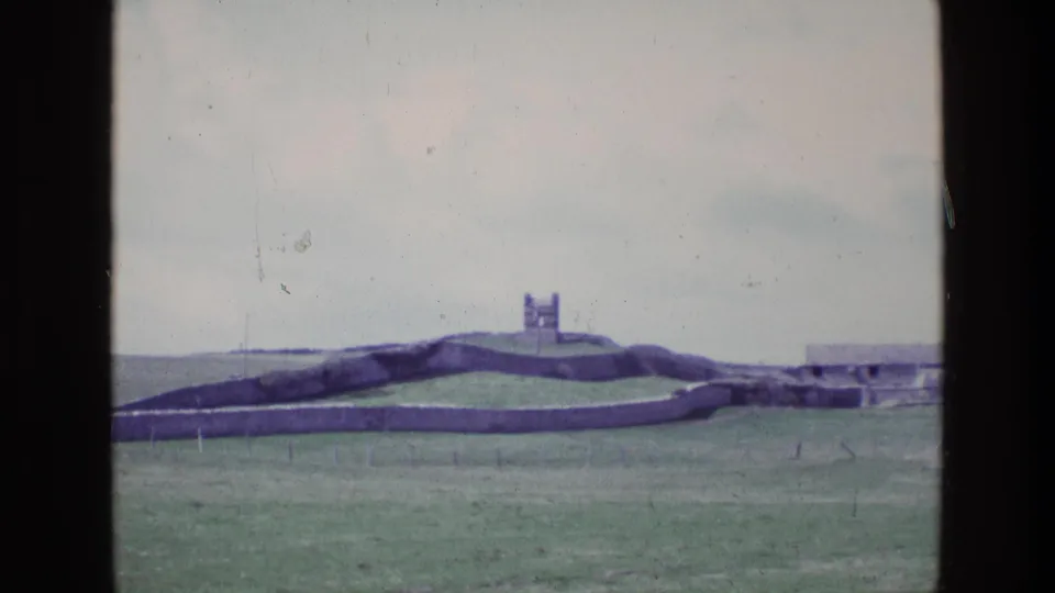 1969 Ireland landscape frame with rolling grass, low stone walls, a small distant tower, and a low structure at right.