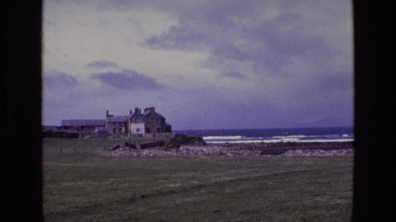 Closer coastal view of house and outbuildings beside rocky shore and breaking waves.