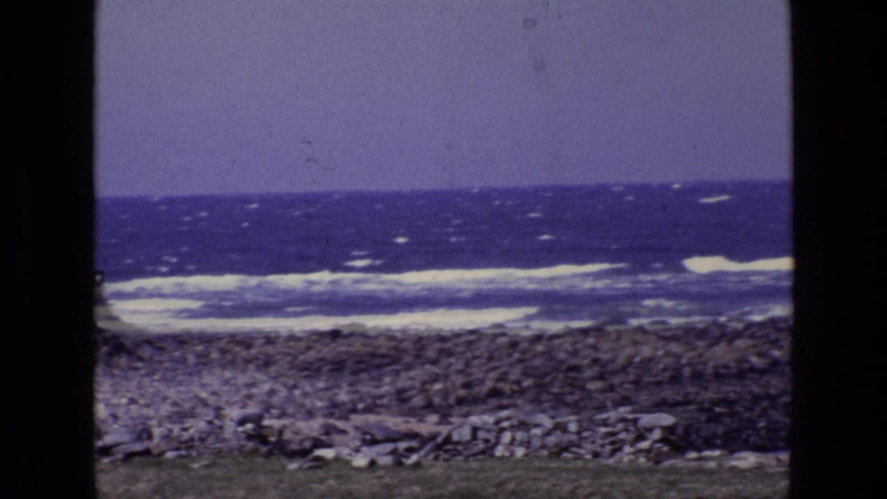 Vintage 8mm view of an Irish rocky shore with white-capped waves and a purple-blue sky, framed by dark film edges.