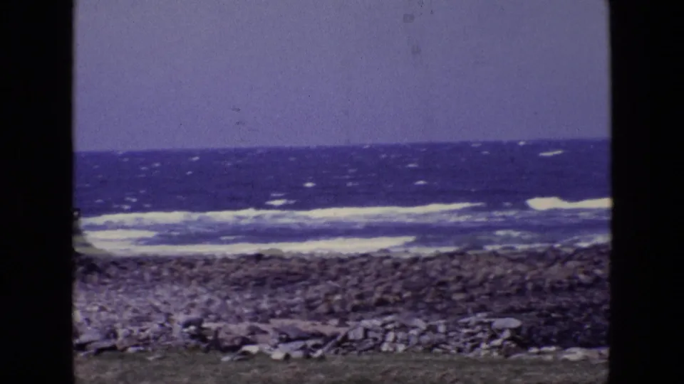 Vintage 8mm view of an Irish rocky shore with white-capped waves and a purple-blue sky, framed by dark film edges.