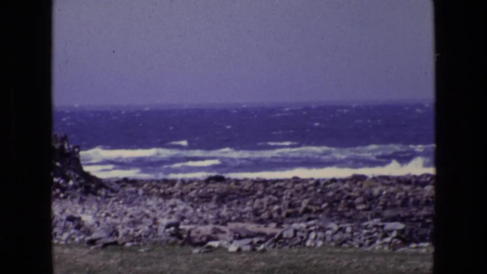 Aged 8mm coastal frame from Ireland showing choppy sea, white surf, rocky foreground, and pronounced dark frame borders.