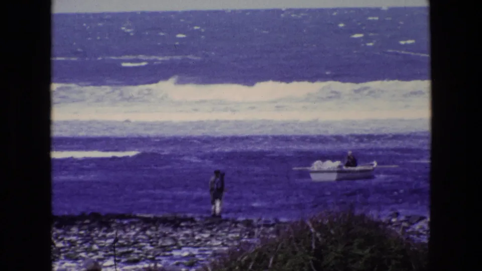 Vintage 8mm frame from Ireland showing a lone shoreline figure and a small boat set against white surf.