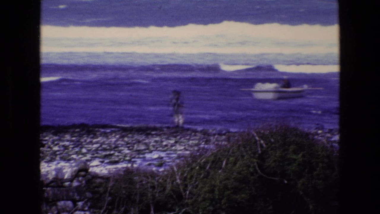 Lone person on a rocky shore watching a small boat in blue ocean waves.
