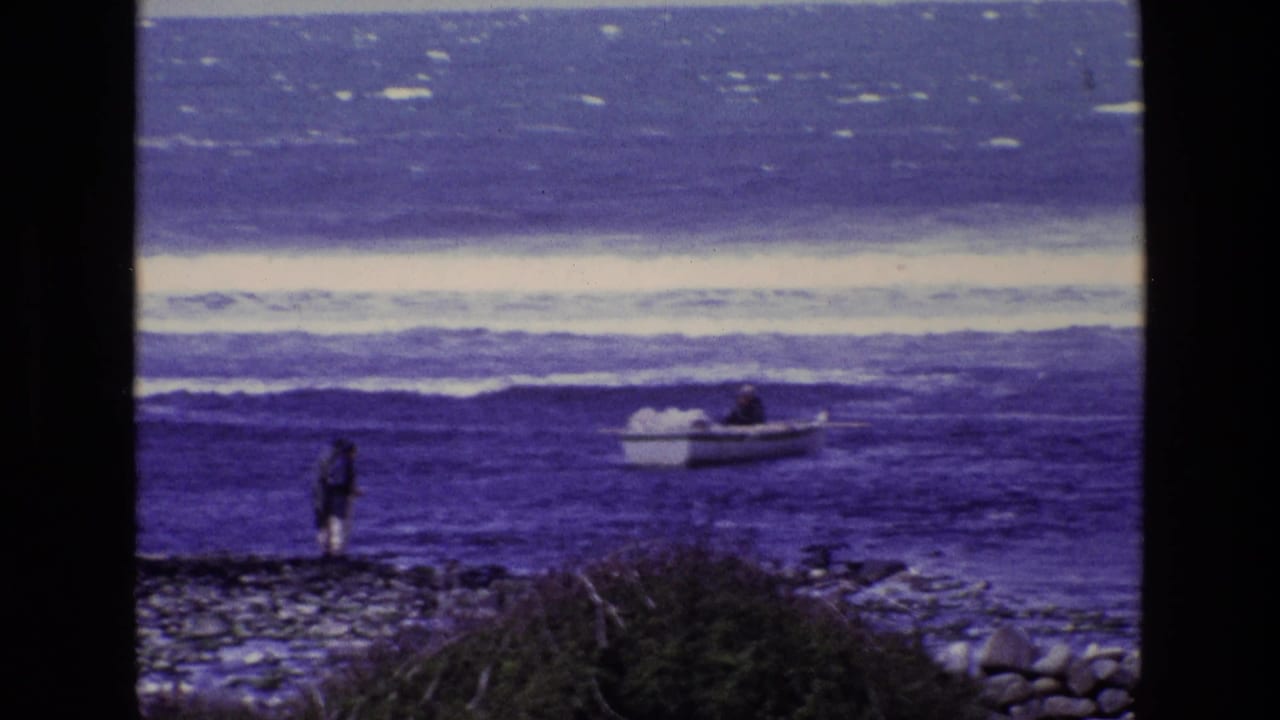 Lone figure on a rocky shore watching a small boat near ocean waves.