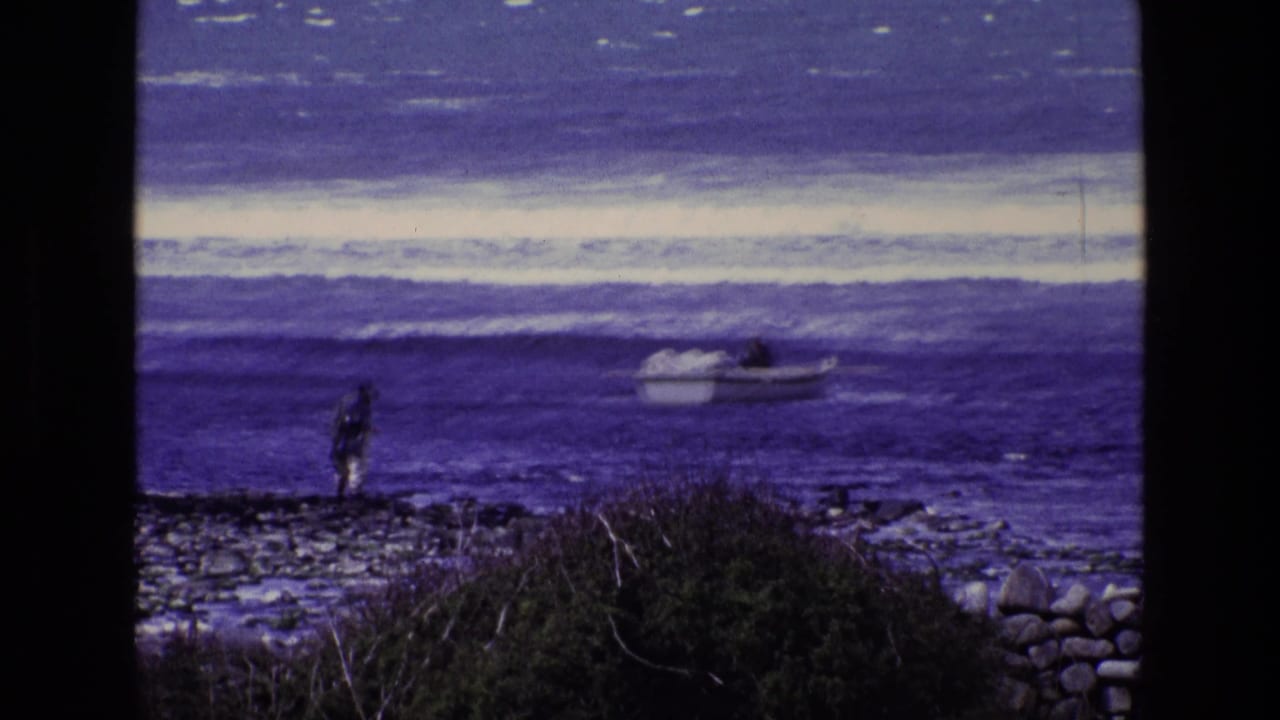 Rocky shoreline with a standing figure and small boat offshore.