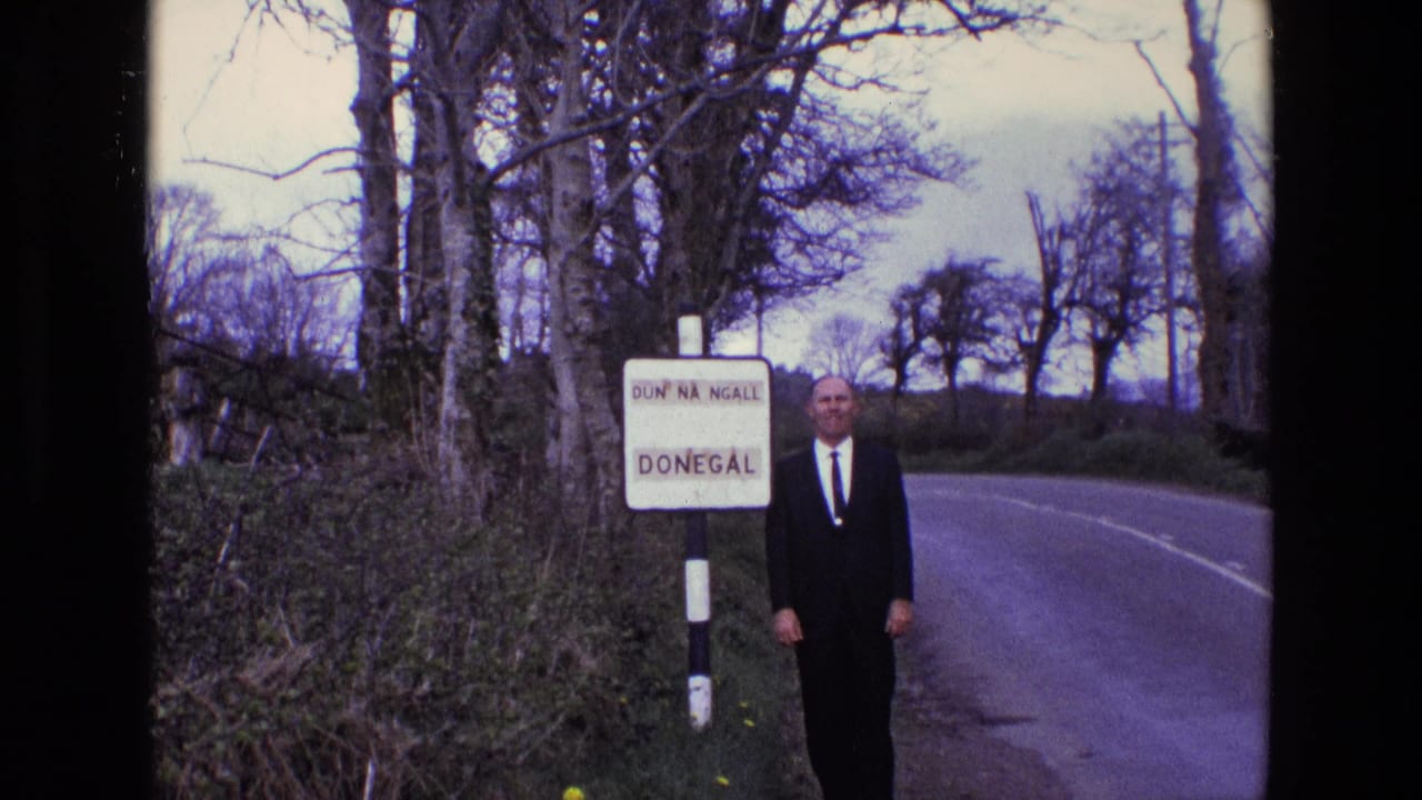 Man in a dark suit stands beside a Donegal road sign on a rural roadside.