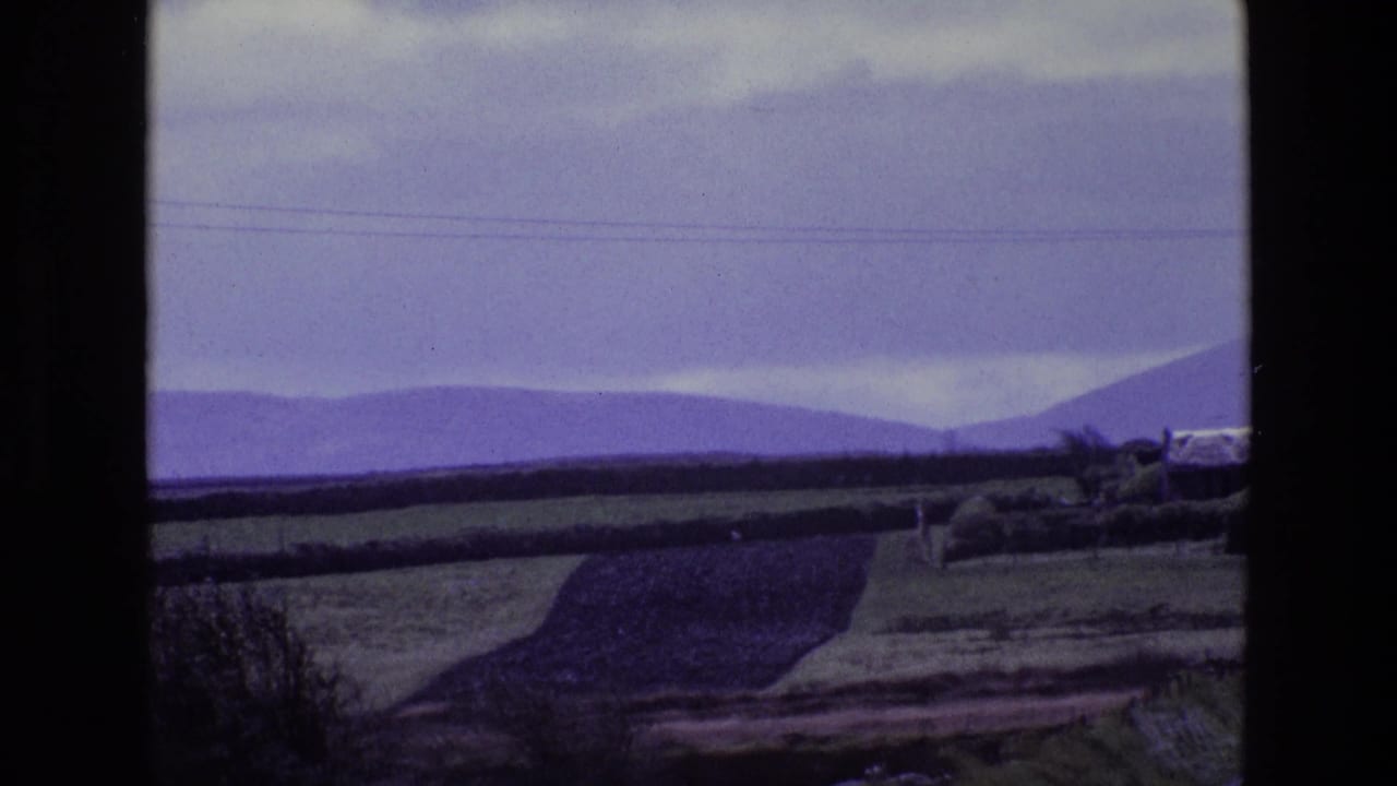 Wide rural landscape with fields, hedgerows, distant hills, and cloudy sky.