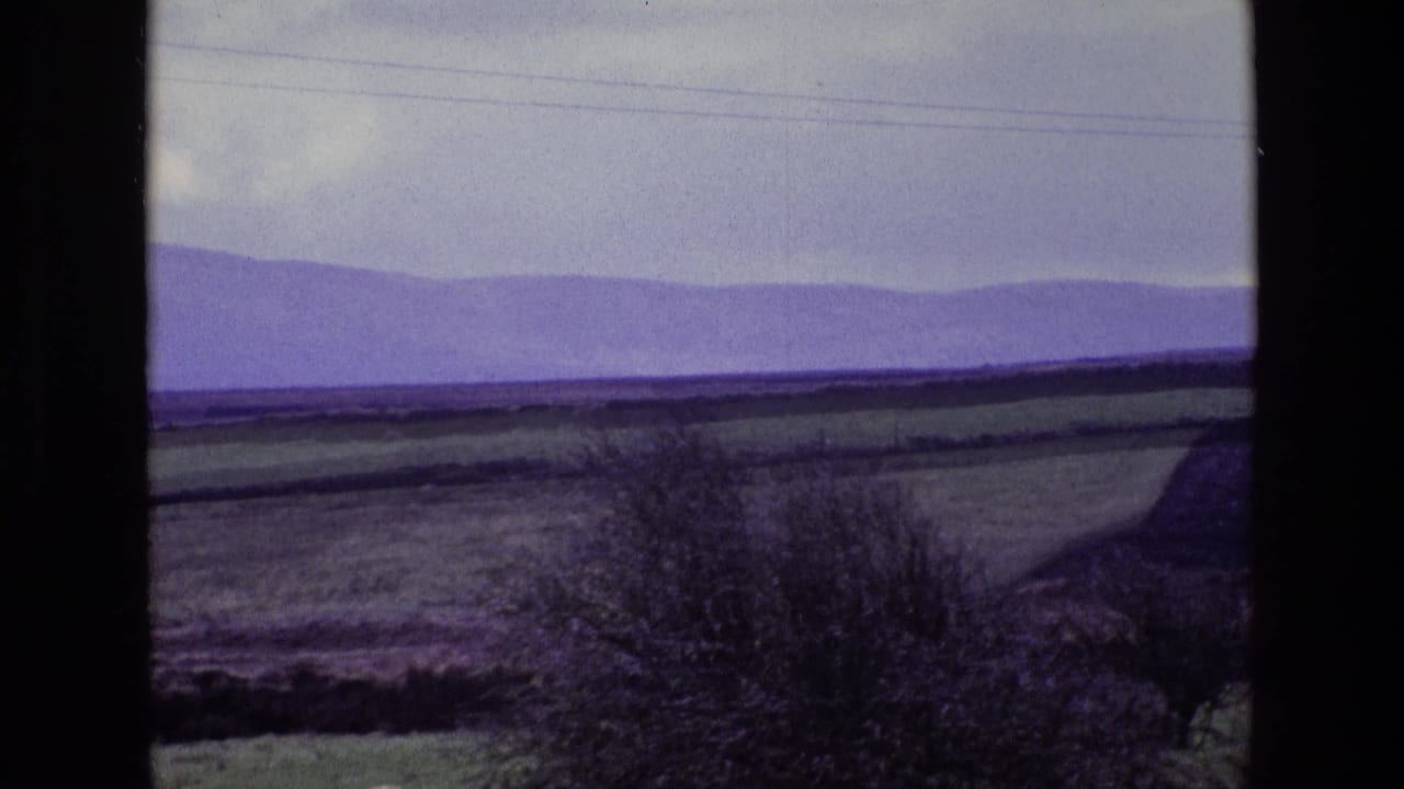 Rolling fields and distant purple mountains under a cloudy sky, with power lines across the horizon.