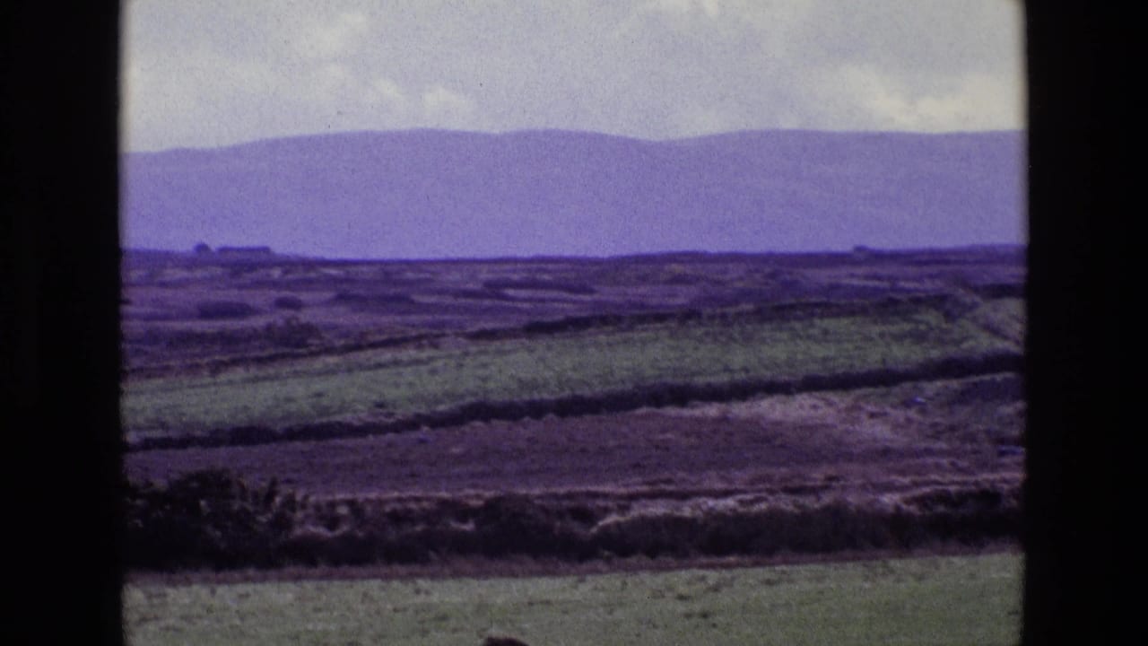 Open fields and low distant hills viewed through dark vertical borders beneath gray clouds.
