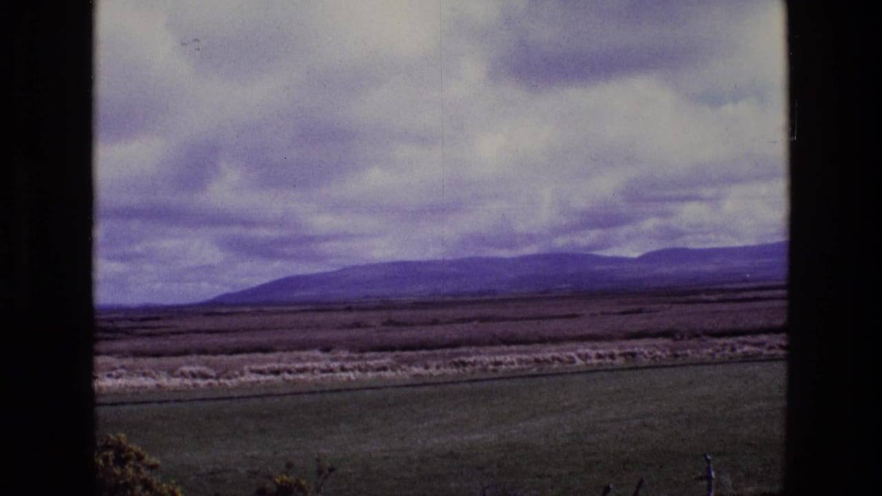 Rural fields with a distant mountain range under a cloudy sky.