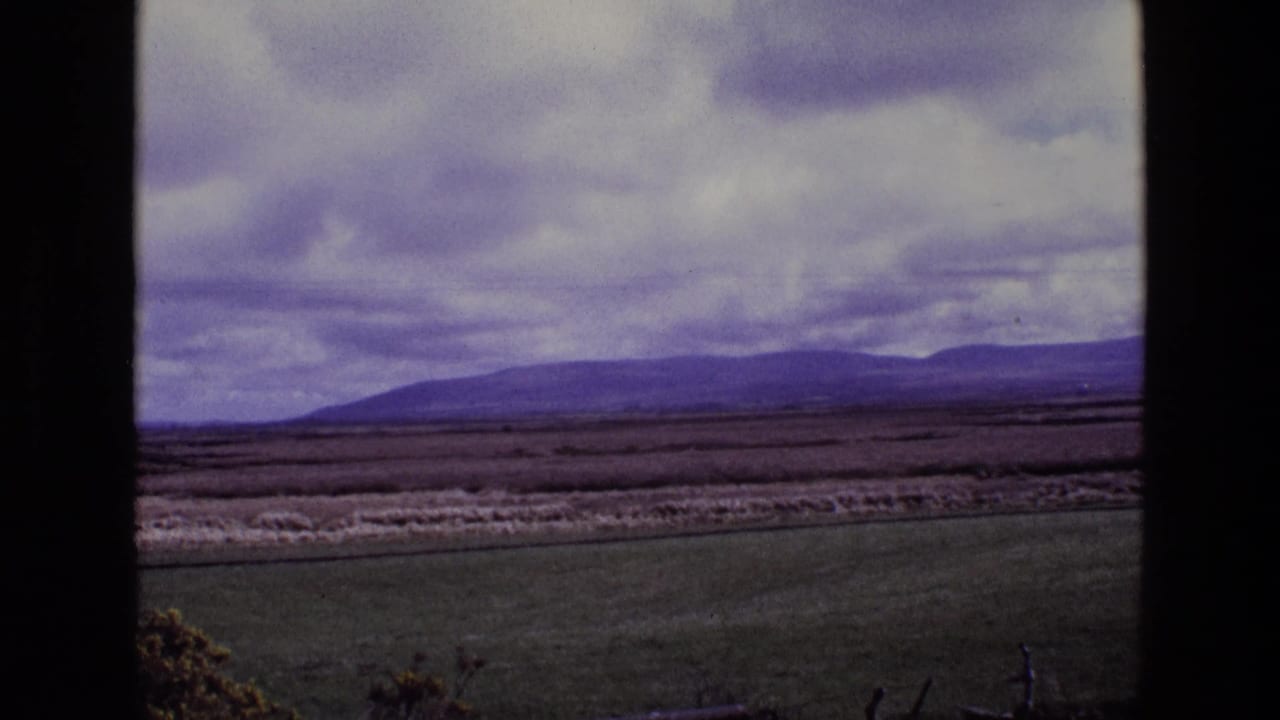 1969 Ireland landscape frame with green foreground, darker midground, distant mountains, and mottled cloud cover.