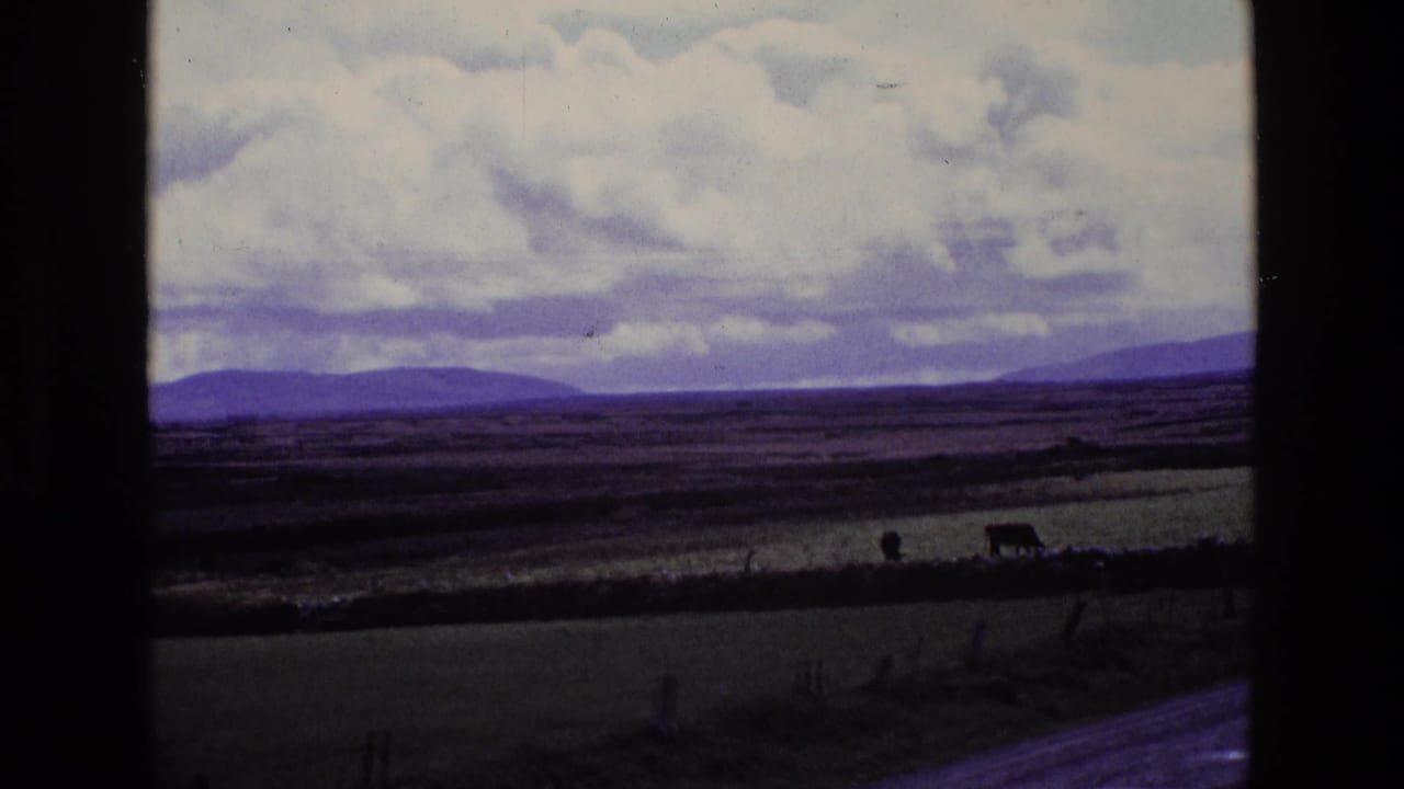 1969 Ireland countryside view with fields, low hills, a cloudy sky, and a dark vertical window frame crossing the shot.