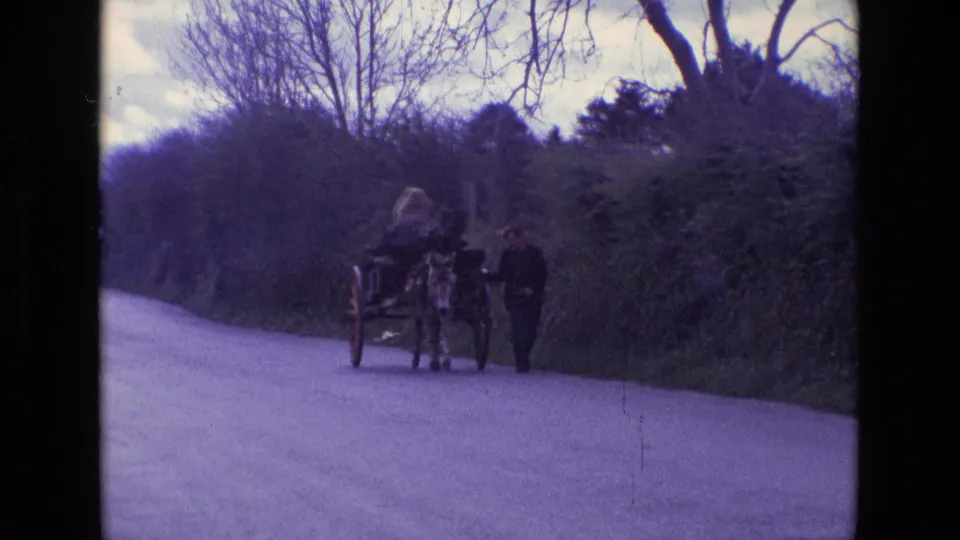 1969 Ireland rural road scene with a donkey-drawn cart, seated woman, and man walking beside the animal.
