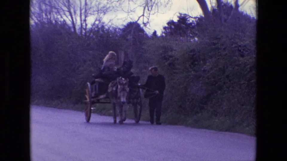 1969 Ireland frame showing the donkey cart approaching, with the woman seated high and the man walking at the side.