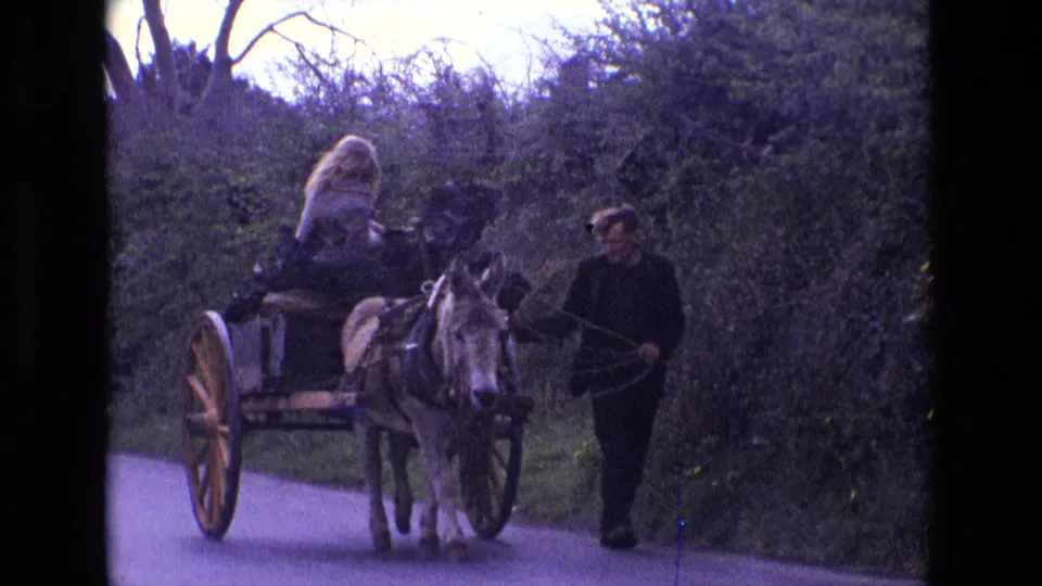 A closer 1969 Ireland frame shows the donkey-drawn cart, seated blonde passenger, and man walking beside the animal on the rural lane.