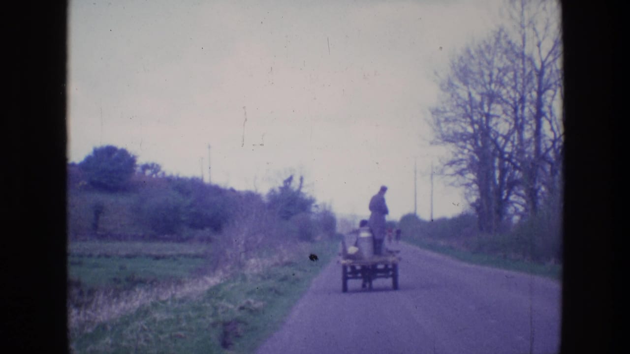 Small cart continues down the road with a man standing on it.