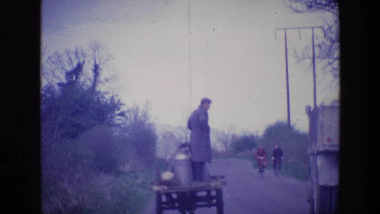 1969 Ireland home-movie frame showing a man on a small wooden cart beside a country road with cyclists farther ahead.