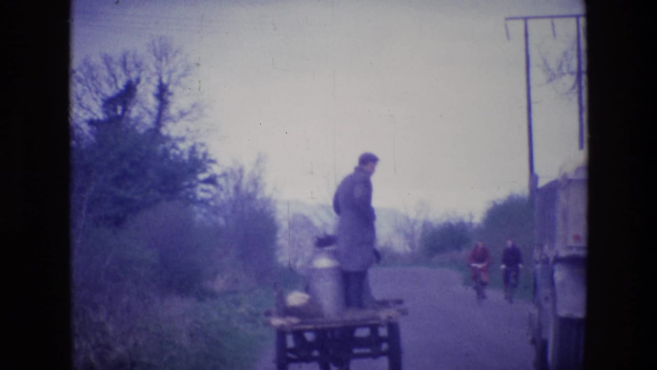 1969 Ireland rural road scene with a man standing on a cart, cyclists in the distance, and a truck entering the frame.