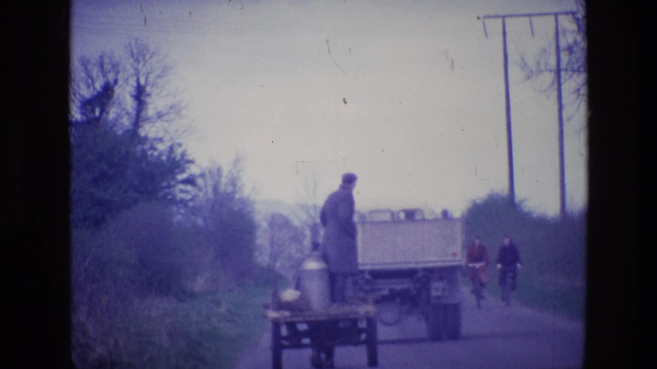 1969 Ireland 8mm frame showing a man on a wooden cart near a truck, with two cyclists behind on a narrow rural road.