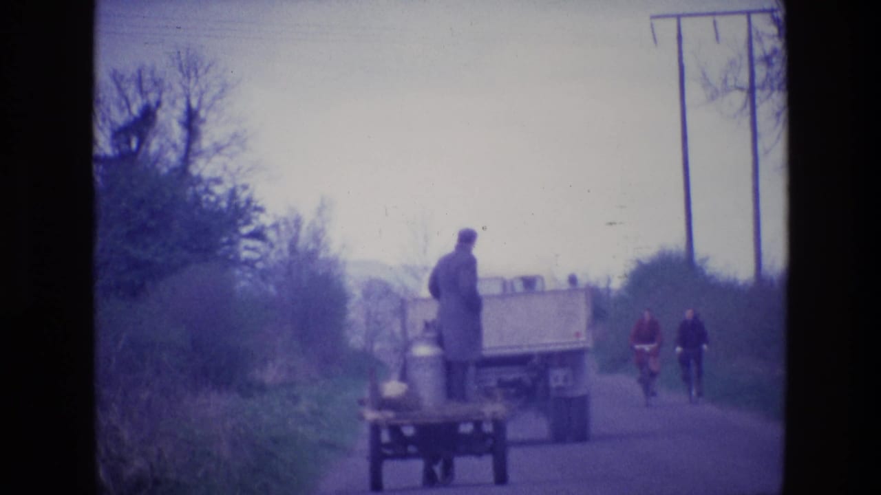 1969 Ireland 8mm frame with a truck and cart on a country road, two cyclists behind, and utility poles beside hedgerows.