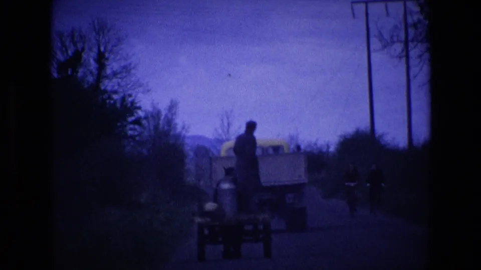 Underexposed 1969 Ireland 8mm frame showing the cart, truck, standing man, and cyclists on a rural road.
