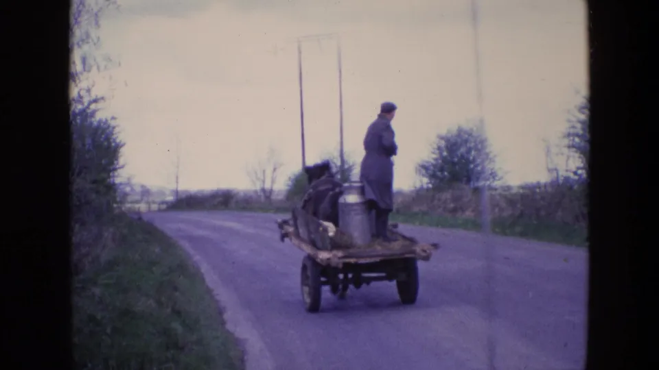1969 Ireland frame showing the milkman and horse cart at greater distance on a quiet countryside road under an overcast sky.