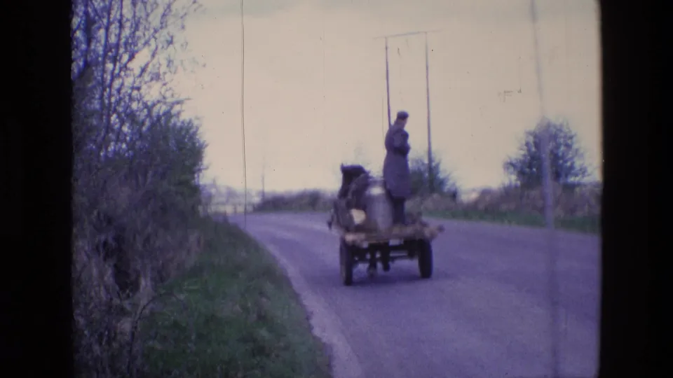 Rear view of the horse-drawn wagon in rural Ireland, with the rider standing near a metal churn as the cart follows the lane.