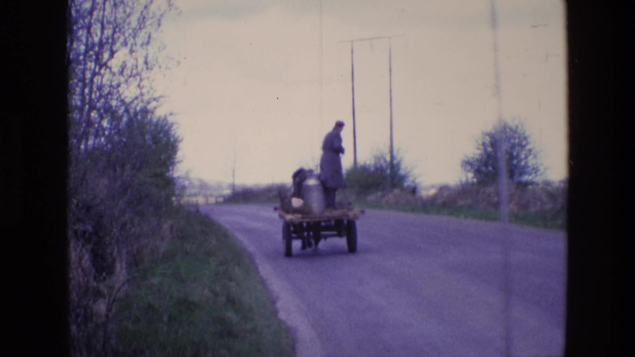 Milk delivery cart continues along the road with a man standing aboard.