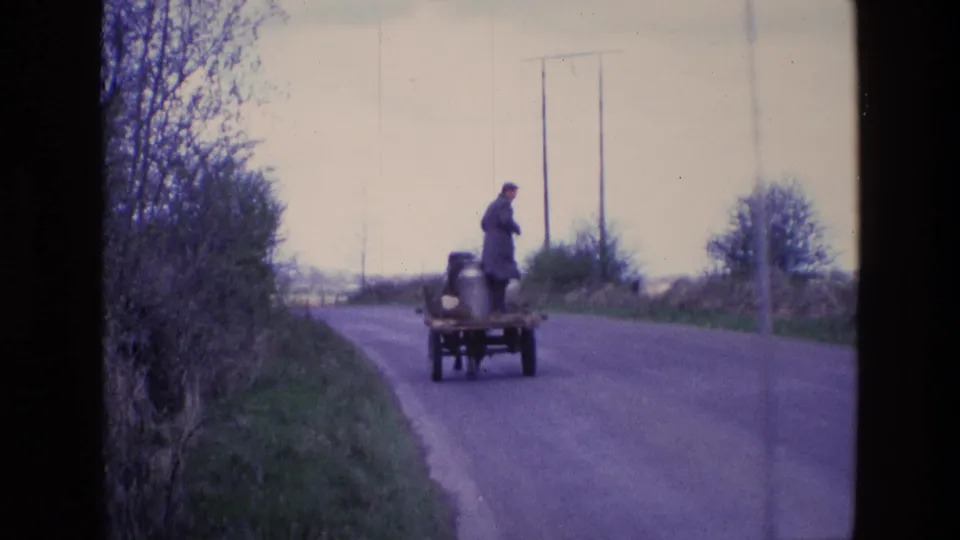 8mm frame of a man on a horse-drawn milk cart carrying metal cans along a rural Irish road in 1969.