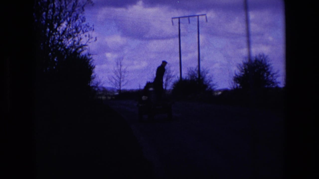 1969 Ireland 8mm frame showing a distant dark figure and small cart on a rural road with telegraph poles and bare trees.