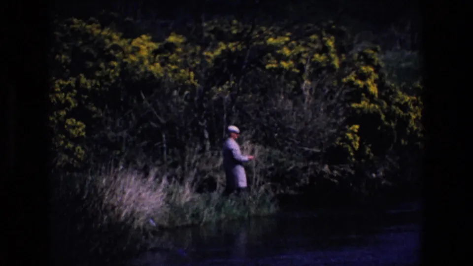 A shadowed 8mm view shows the fisherman standing near the waterline with dense Irish riverside vegetation behind him.