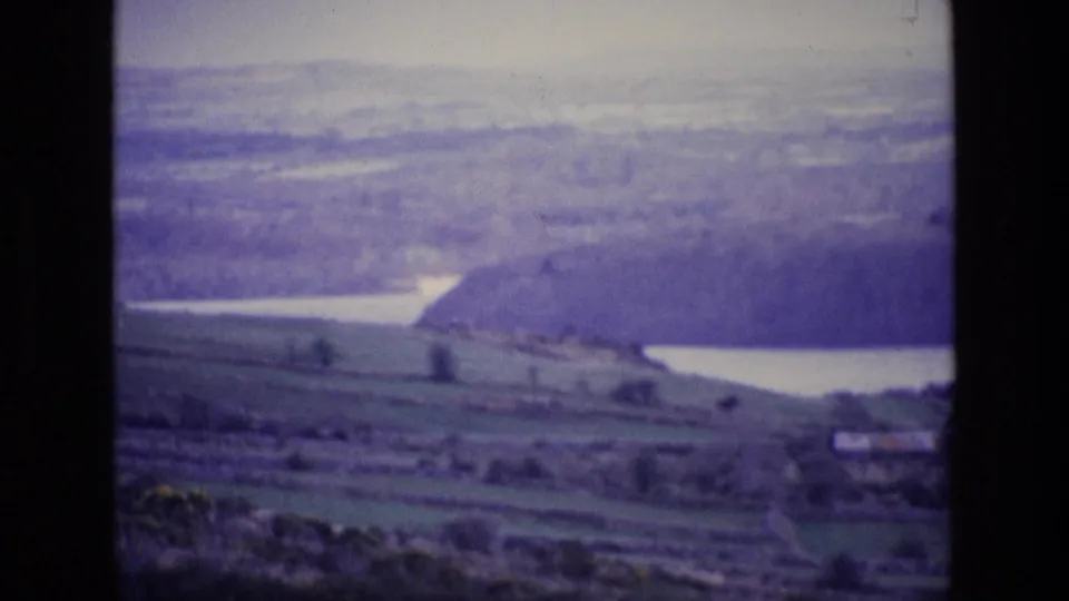 A hazy 1969 Irish countryside view shows rolling fields, distant hills, and water beyond the fishing scene.