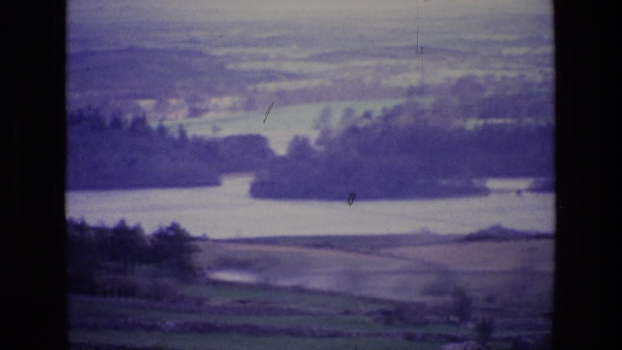 1969 8mm view of an Irish rural river valley with patchwork fields, dark tree lines, and soft distant hills.