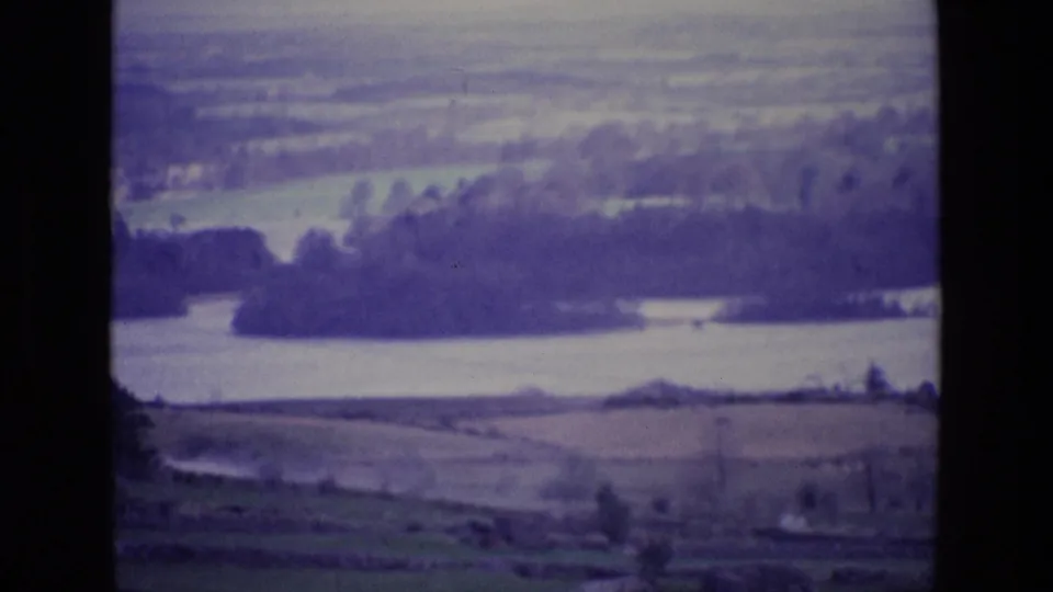 Aged 8mm frame of rural Ireland with river water, tree masses, field boundaries, and muted purple-blue color shift.