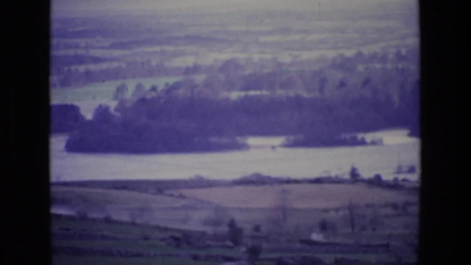 1969 Irish countryside panorama on 8mm film, showing a low river valley, rural fields, trees, and hazy hills.