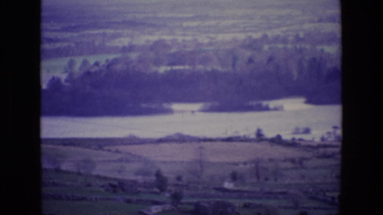 1969 Ireland home-movie frame from a plane, looking across rural fields toward a lake or wide waterway.