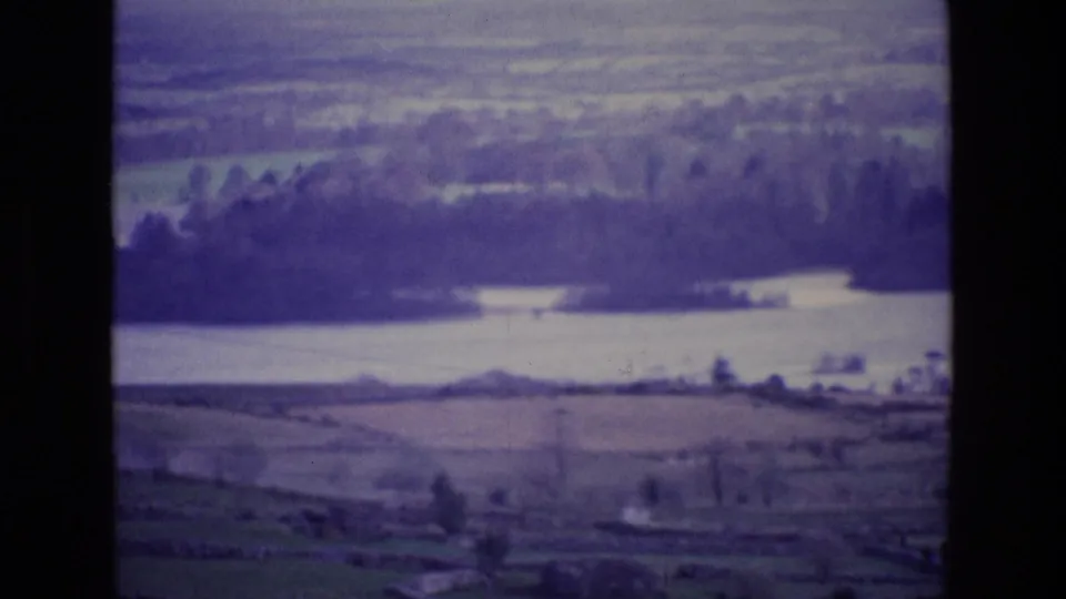 1969 Ireland home-movie frame from a plane, looking across rural fields toward a lake or wide waterway.