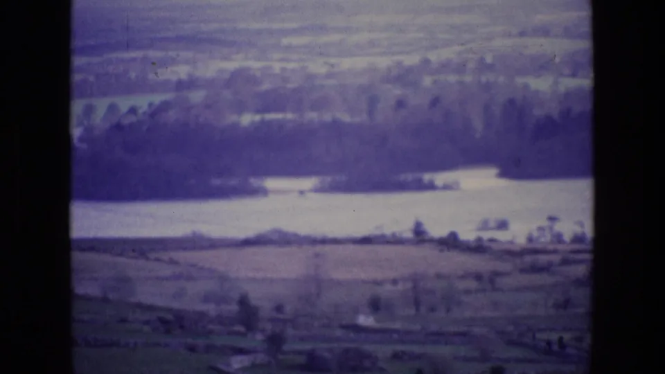 Ireland 1969 aerial home-movie view with water, wooded banks, and fields softened by motion blur and aged color.