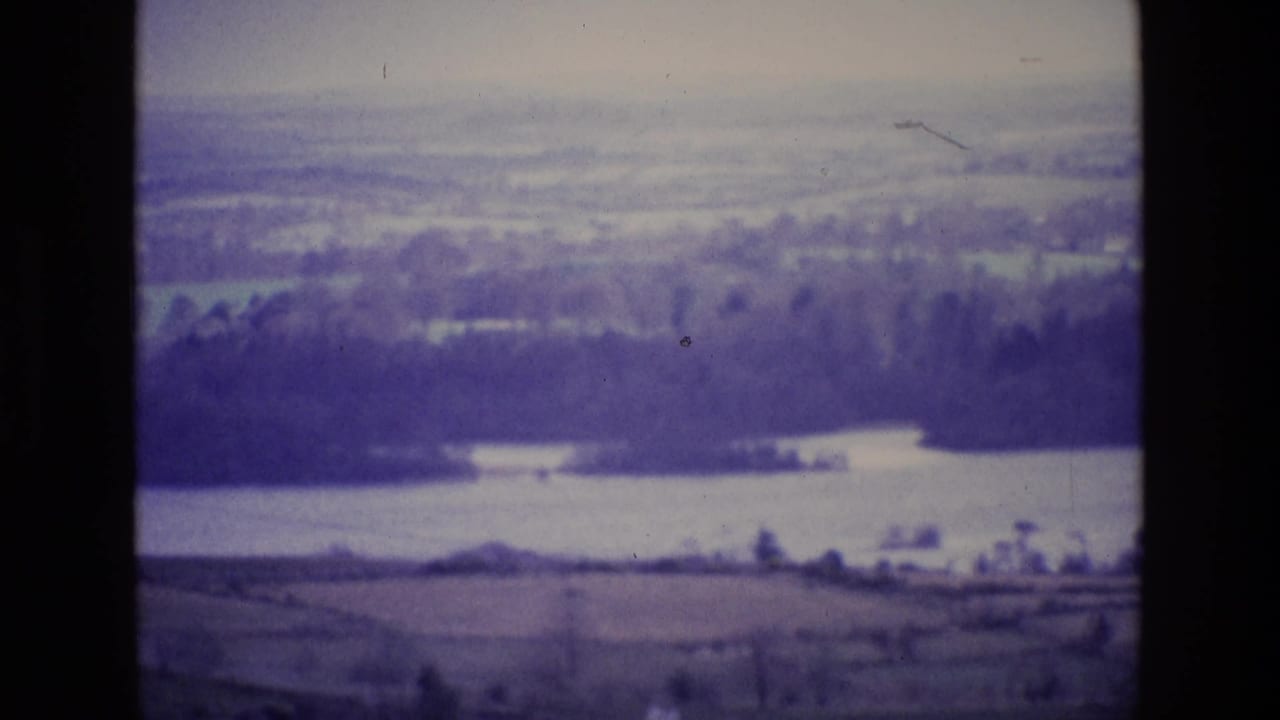Soft hazy view over fields, trees, and a lake, framed by dark film borders.