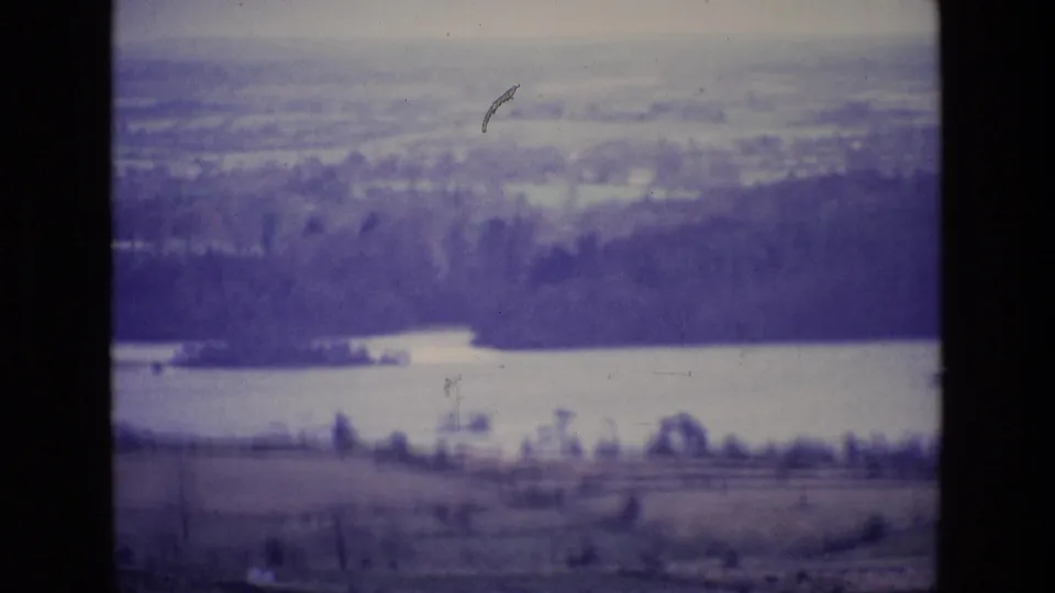 1969 Ireland 8mm frame showing a broad lakeside landscape with trees, fields, haze, and aged-film texture.