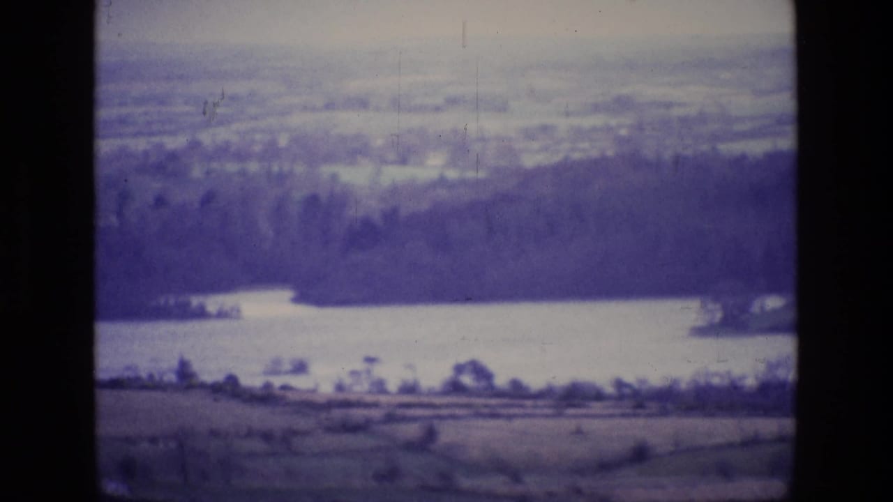 Distant lake below a tree line and hazy countryside, bordered by black film edges.