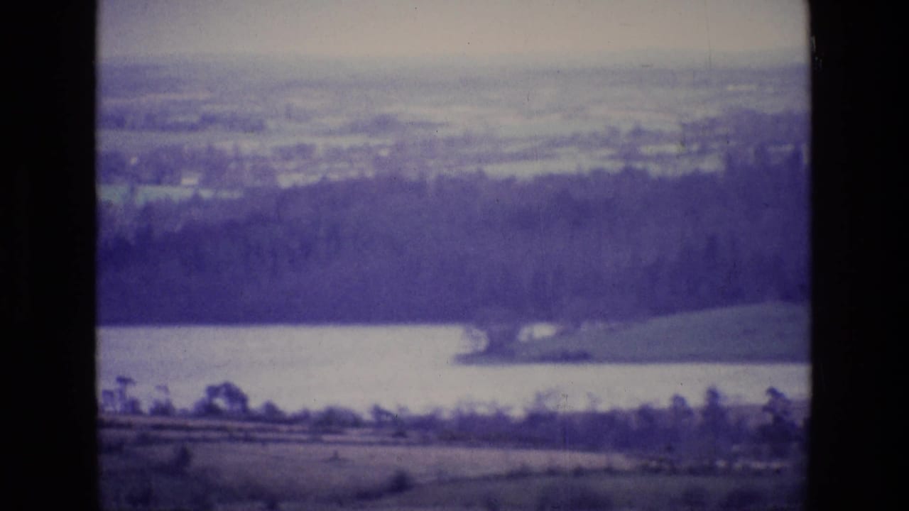Wide lake and wooded ridge seen through a soft, purple-tinted 8mm frame.
