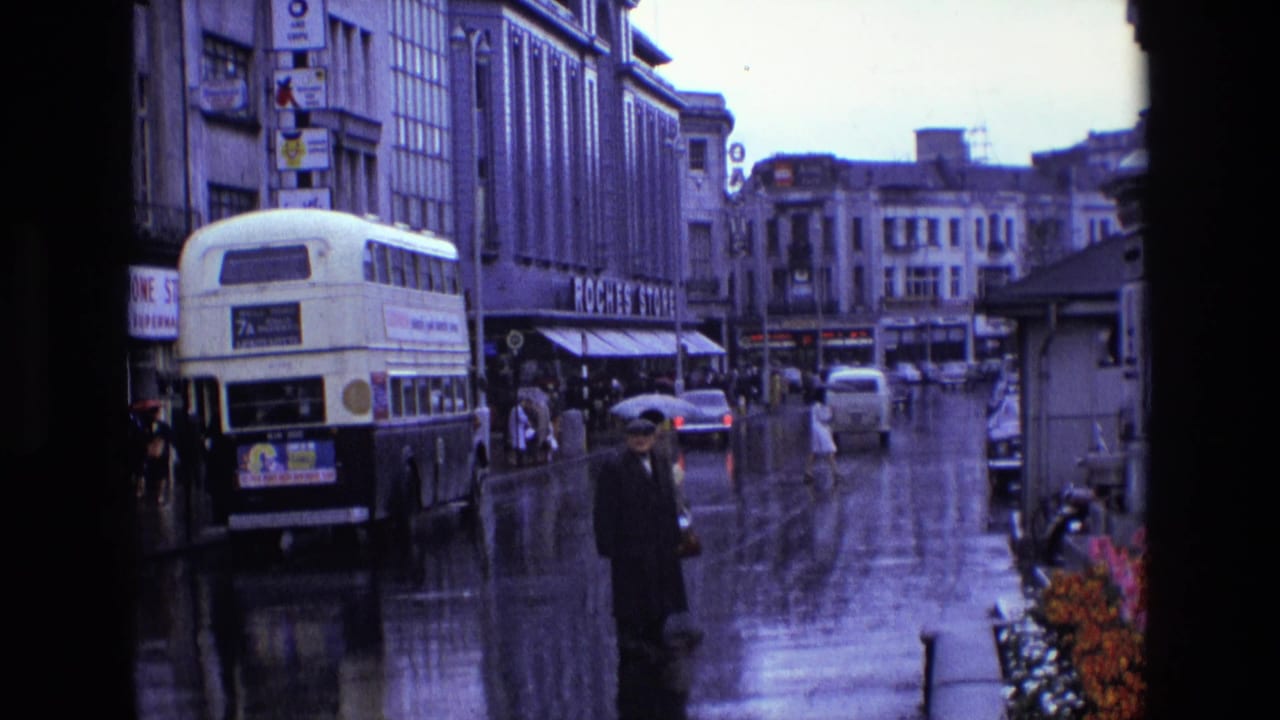 1969 Ireland street scene with a double-decker bus, pedestrians in rainwear, wet road surface and Roches Stores signage.