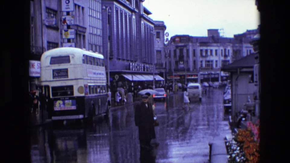 1969 Ireland street scene with a double-decker bus, pedestrians in rainwear, wet road surface and Roches Stores signage.