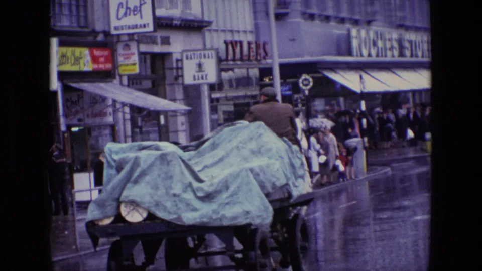 Horse-drawn cart moving past National Bank and other shop signs on a rainy Irish street in the 1969 footage.