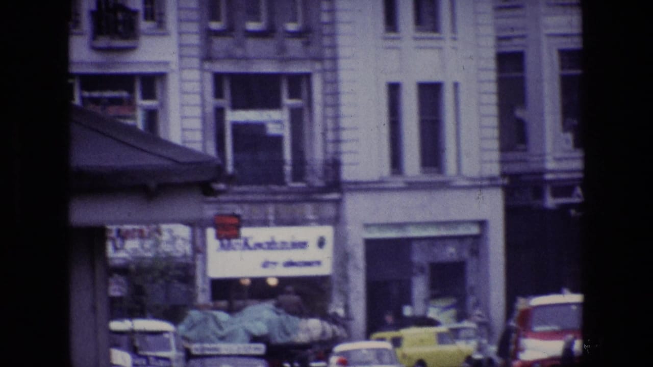 1969 Ireland street traffic with wet roadway, yellow van, red-and-white truck, classic cars and visible shop signage.