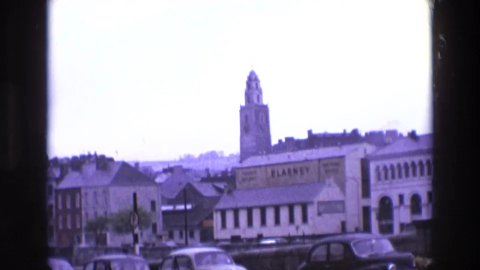 Irish town view with a clock tower, rooflines, parked cars, and a prominent BLARNEY sign below the skyline.
