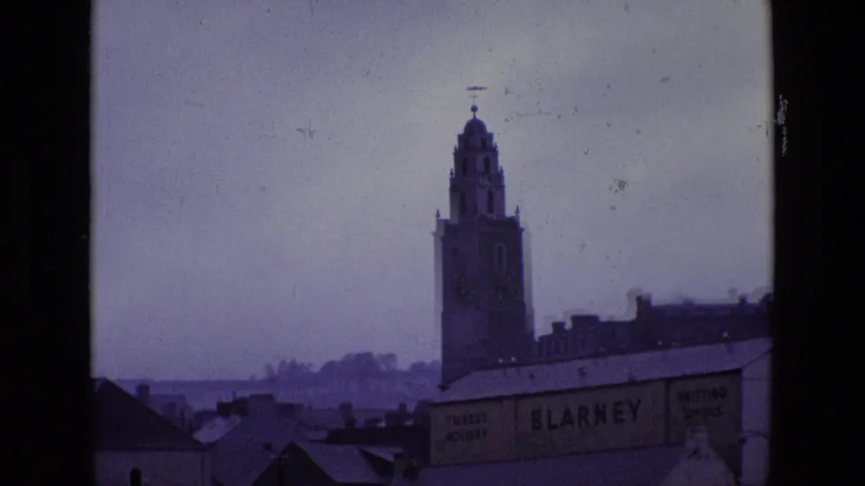 Clock tower and rooftops in an Irish town, with the BLARNEY sign visible on a building below in overcast conditions.