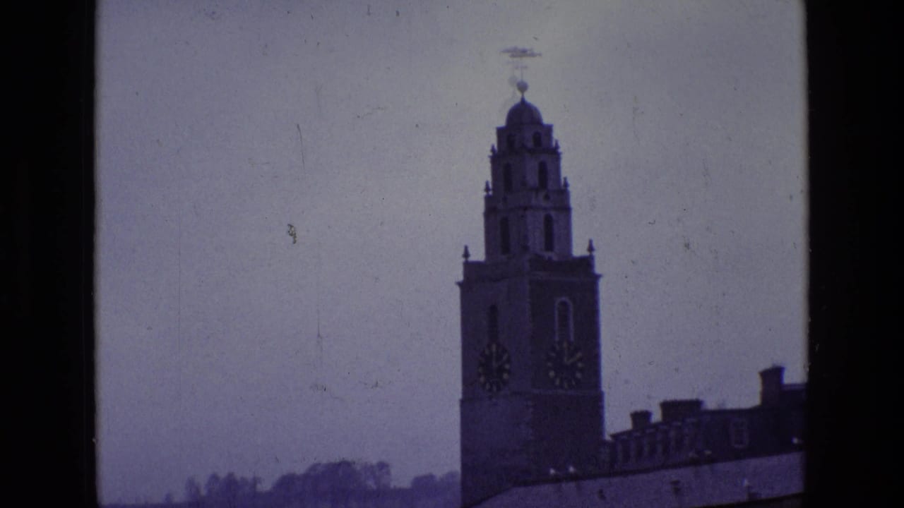 Distant clock tower with roofline below and pale sky behind it.