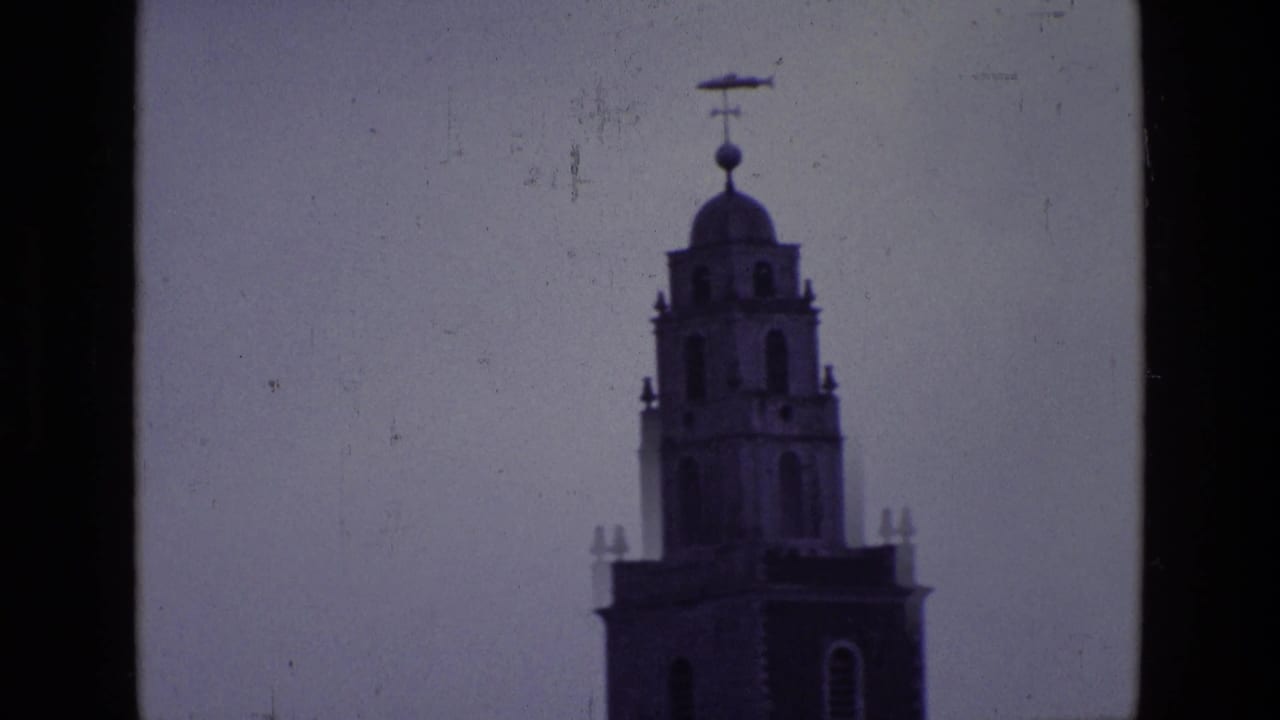 1969 Ireland 8mm frame isolating the upper clock tower, with domed top, weather vane, and soft home-movie exposure.